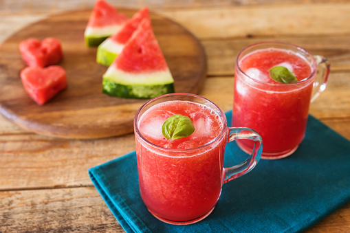 watermelon pieces on wood plate with two glasses of watermelon smoothie - juice with ice, close up