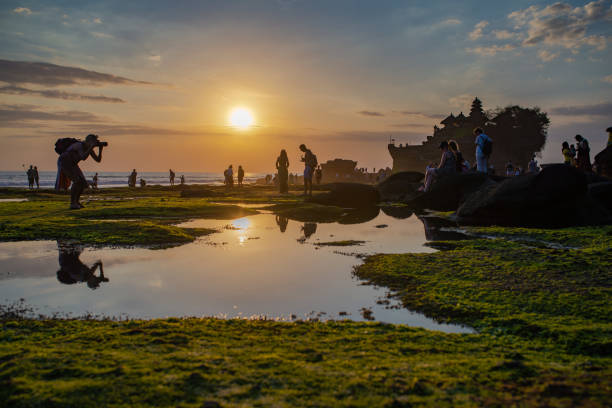 Visitors are enjoying sunset at Tanah Lot temple, Bali, Indonesia Tanah Lot, Bali, Indonesia - September 7, 2017: Visitors are enjoying sunset at Tanah Lot temple. Taken at sunset with reflection of sky and people in low tide ponds. tanah lot sunset stock pictures, royalty-free photos & images