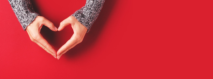 Female hands in shape of heart on red background. Healthcare, love and Valentine's Day concept. Banner for website.