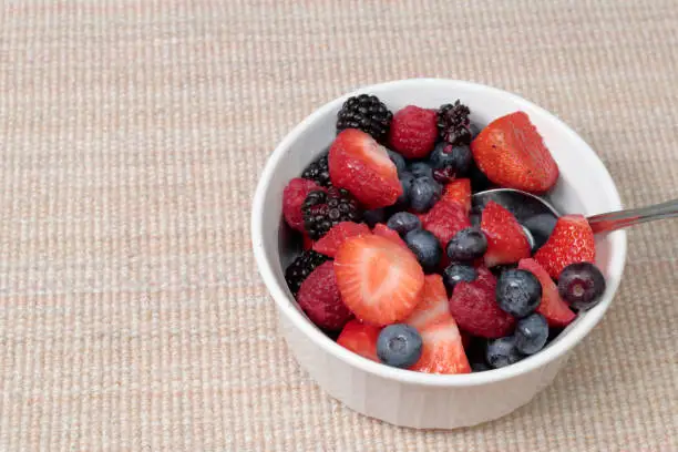 Sweet organic fruit healthy food variety of berries bowl and spoon. Round bowl of mixed berries and shiny silver spoon of blueberries, blackberries, strawberries and raspberries on a brown placemat.