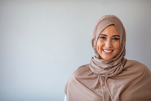 Young asian muslim woman in head scarf smile with arms crossed. Portrait of young muslim woman wearing hijab head scarf at gray background. Portrait of beautiful Muslim woman on grey background