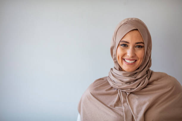 Portrait of young muslim woman wearing hijab head scarf at gray background. Young asian muslim woman in head scarf smile with arms crossed. Portrait of young muslim woman wearing hijab head scarf at gray background. Portrait of beautiful Muslim woman on grey background arab woman stock pictures, royalty-free photos & images