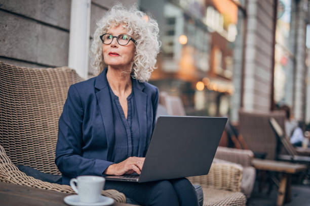 istock Beautiful senior woman working on laptop while drinking coffee 1194747942