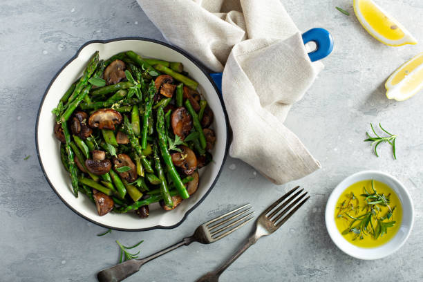 Asparagus and mushrooms in a cast iron pan Asparagus and mushrooms sauteed in a cast iron pan with lemon zest sauteed stock pictures, royalty-free photos & images