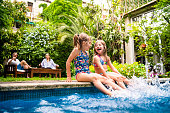 Two little girls sitting at poolside and splashing water with legs