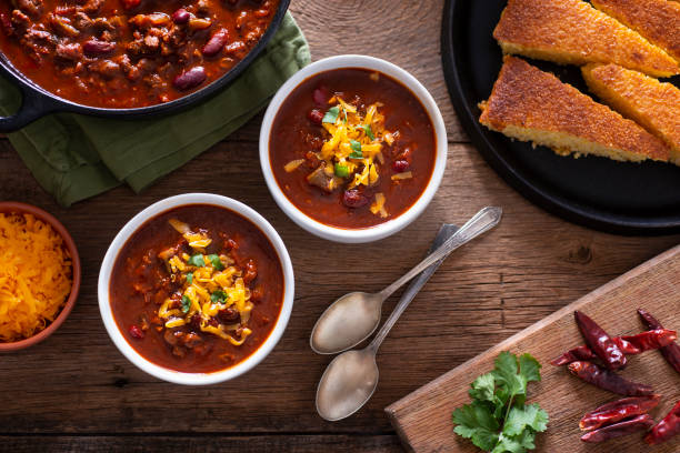 Chile Bowls of Homemade Chili with Corn Bread, Cilantro and Cheddar Cheese chili pepper photos stock pictures, royalty-free photos & images