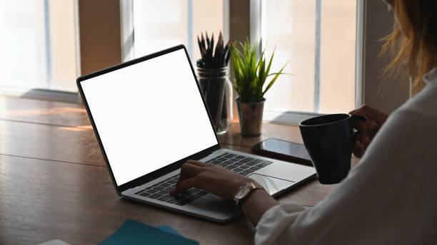 istock Cropped shot woman using her laptop and holding coffee with empty screen computer. 1194812986