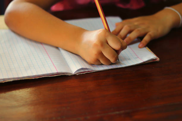 istock Young hand writing a lesson with a pencil on a book on wooden table - educational concept 1194816309