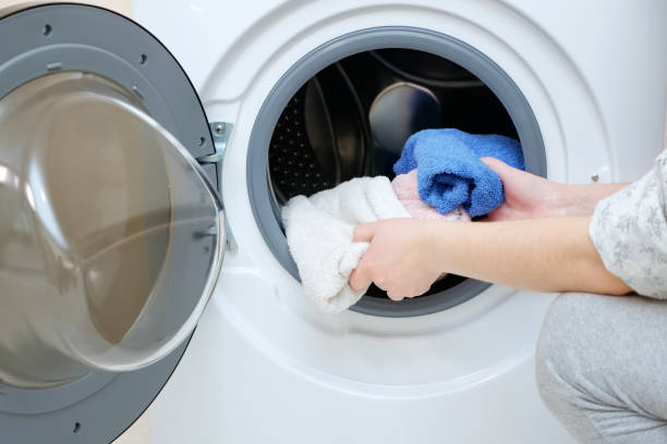 istock woman loading dirty towels into washing machine closeup 1194820028