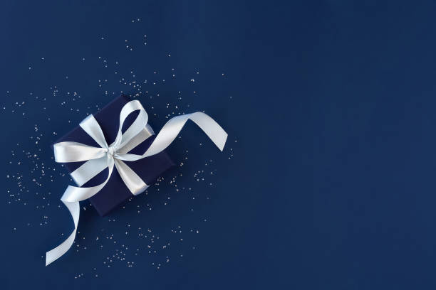 boîte de cadeau avec l'arc et les confettis sur le fond bleu. vue du haut. laïc plat - blue plate photos et images de collection