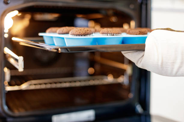 Woman taking baked muffins out of oven in domestic kitchen, using oven mitt