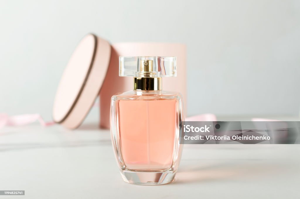 Close up of glass bottle of perfume and opened gift box as a background on the white surface Close up of glass bottle of perfume and pink round gift box on the white surface against white background Perfume Stock Photo
