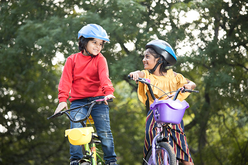 Carefree brother and sister with arms outstretched on bicycle at park