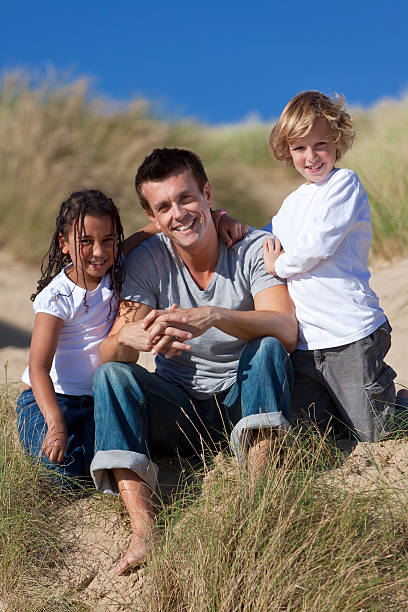 istock Father, Son & Mixed Race Daughter Sitting on Beach 119482696