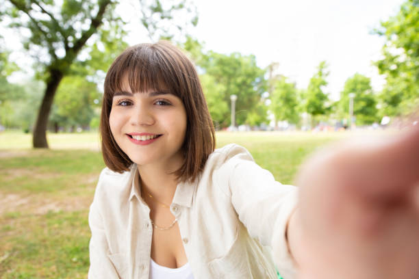 istock Cheerful young woman taking selfie in park 1194828840