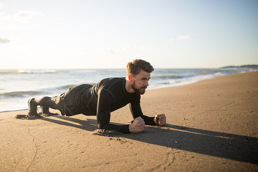 Young bearded men is doing basic plank exercise at the beach