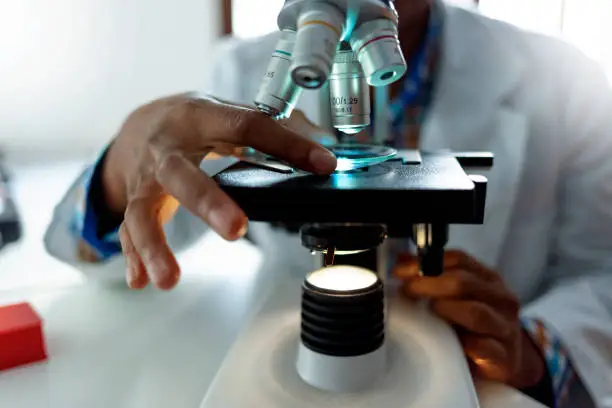 Photo of African-American scientist looking in microscope while working on medical research in modern laboratory.