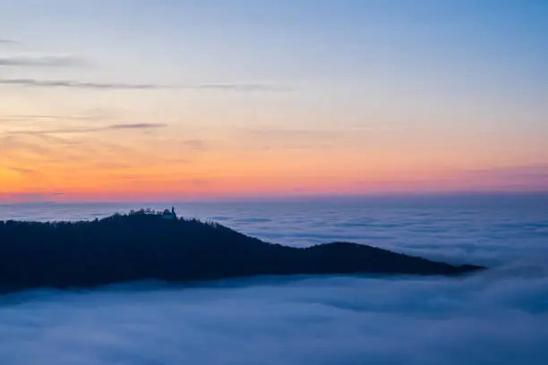 Germany, Magical aerial view above fog clouds surrounding castle teck on teckberg mountain in swabian jura nature landscape at sunset near stuttgart