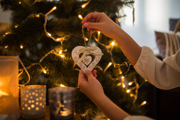 istock Woman hands decorating christmas tree with heart shaped white ornament 1194833764