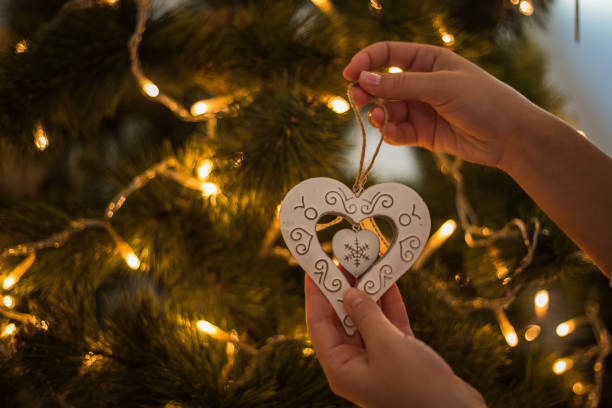 Woman hands decorating christmas tree with heart shaped white ornament