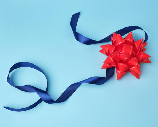 istock blue silk thin ribbon twisted and red shiny bow on a blue background 1194833912