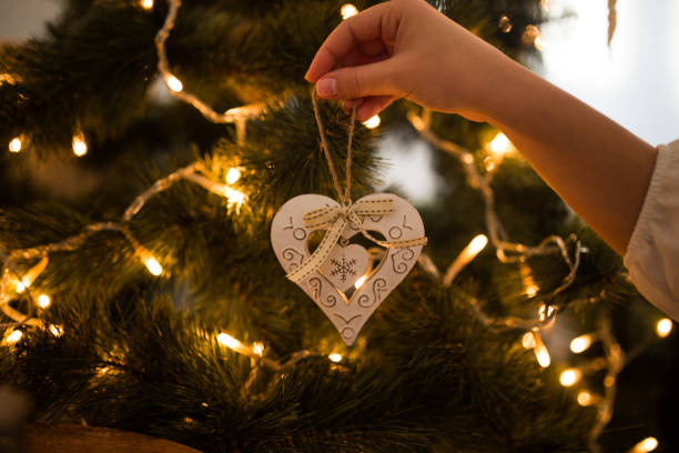 istock Woman hands decorating christmas tree with heart shaped white ornament 1194833937
