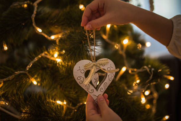 istock Woman hands decorating christmas tree with heart shaped white ornament 1194833955