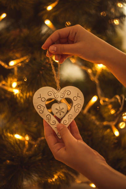 istock Woman hands decorating christmas tree with heart shaped white ornament 1194834057