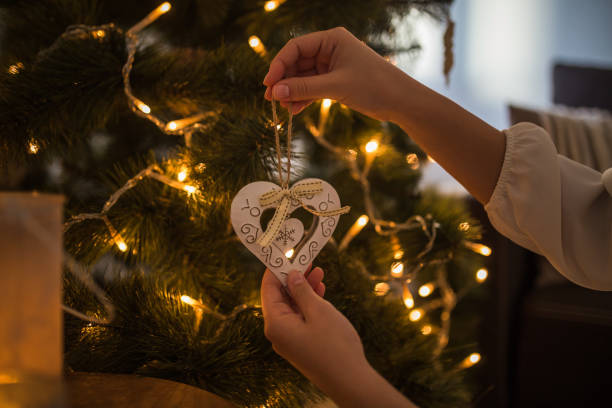 istock Woman hands decorating christmas tree with heart shaped white ornament 1194834075