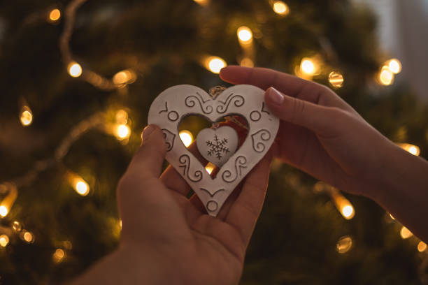 istock Woman hands decorating christmas tree with heart shaped white ornament 1194834788