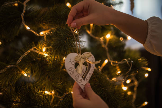 istock Woman hands decorating christmas tree with heart shaped white ornament 1194834812