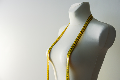 Tailor mannequin with yellow measuring tape on grey background