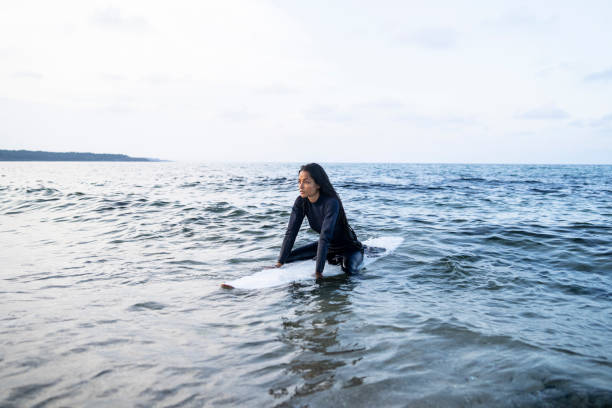 African woman sitting on surfboard in sea stock photo
