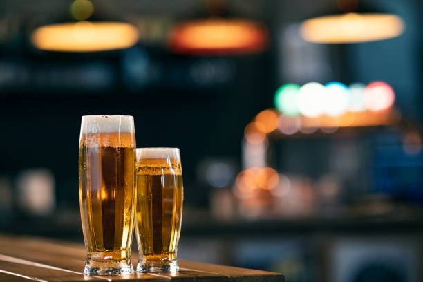 Two draft beer glasses on counter Two glasses full of beer on wooden table with copy space. A pint of draft beer and half cold pint on wooden couter at pub. ale stock pictures, royalty-free photos & images