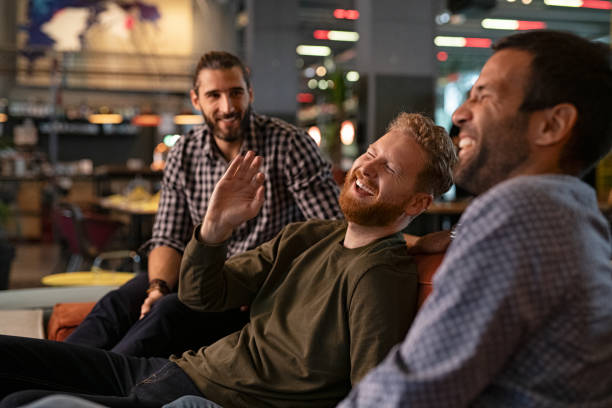Mid adult men friends enjoying at pub Group of three best friends laughing and enjoying the evening at pub. Happy young men enjoying late night staying together at bar. Cheerful guys sitting on couch and having fun while relaxing after work. only men stock pictures, royalty-free photos & images