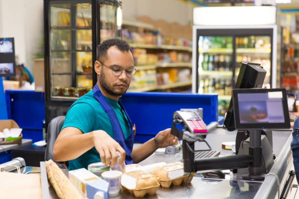 Focused African American cashier scanning goods at checkout Focused African American cashier scanning goods at checkout. Concentrated young man in eyeglasses at workplace. Shopping concept cashier stock pictures, royalty-free photos & images