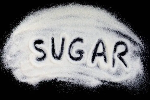 Photo of Word sugar hand lettering on a placer of refined white sugar. Beet sugar on a black background