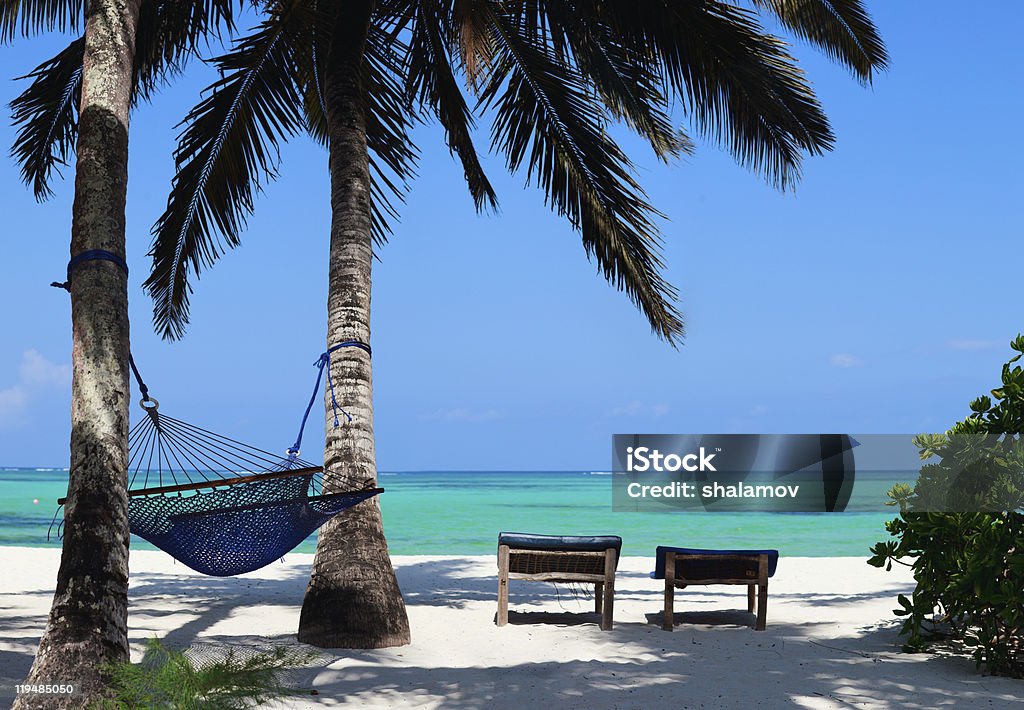 Hammock and sun beds on a perfect tropical beach Perfect tropical beach of Zanzibar island with palm trees, sunbeds and hammock. 3 photos panorama Beach Stock Photo