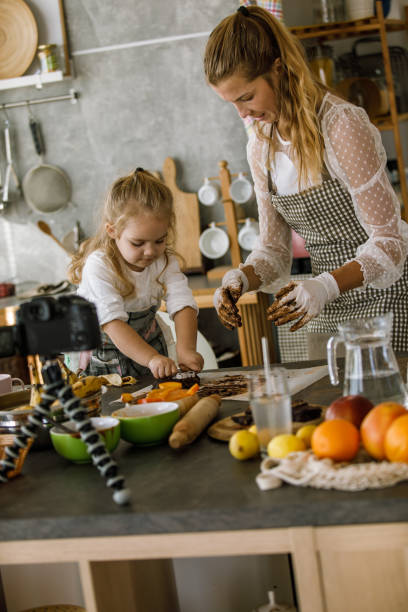 mała dziewczynka pomagająca swojej matce vlogera przygotować ciasteczka - vegan food cheerful vertical indoors zdjęcia i obrazy z banku zdjęć