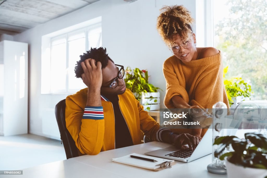 Woman helping colleague in office Businesswoman pointing at laptop and helping coworker working in office. Startup business professionals working together in modern workplace. 30-34 Years Stock Photo