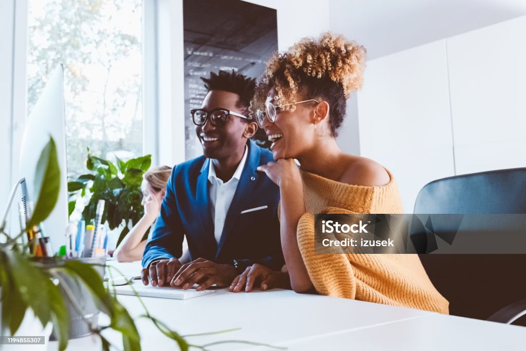 Two business professionals happily working in office Two business professionals looking at computer monitor and smiling. Businessman and businesswoman working together in a new project. Discussion Stock Photo