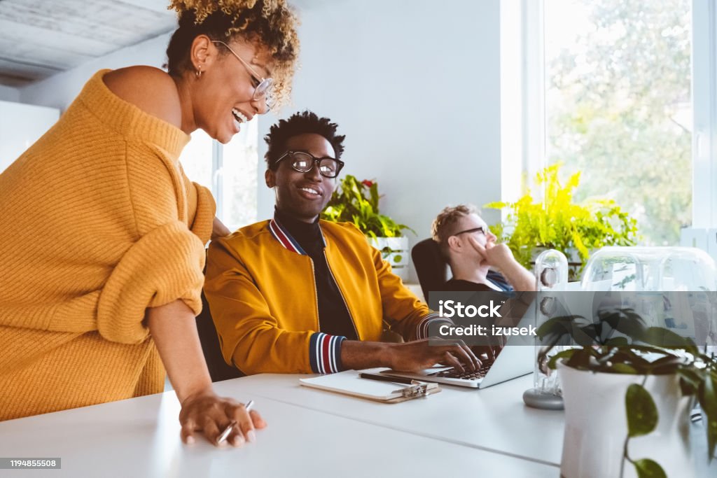 Two business people working together at startup Two business people working together on a project. Businessman working on laptop with female colleague smiling and discussing work in modern office. 30-34 Years Stock Photo