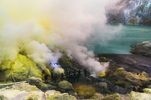 Tourists exploring the beautiful landscape of Ijen volcano and looking at the scenic blue fire and yellow sulfur smoke during sunrise on java island, Indonesia