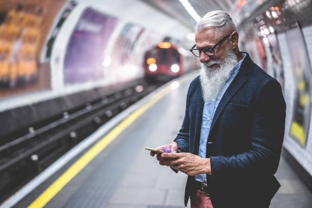 homme de hipster aîné utilisant le smartphone dans le métro - personne mûre de mode ayant l'amusement avec des tendances de technologie attendant son train - concept de mode de vie âgé joyeux - foyer principal sur le visage - subway station subway train new york city people photos et images de collection