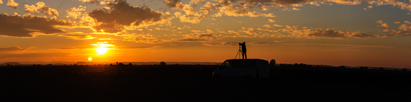 Panoramic of a field sunset with photographer taking pictures on top of the van