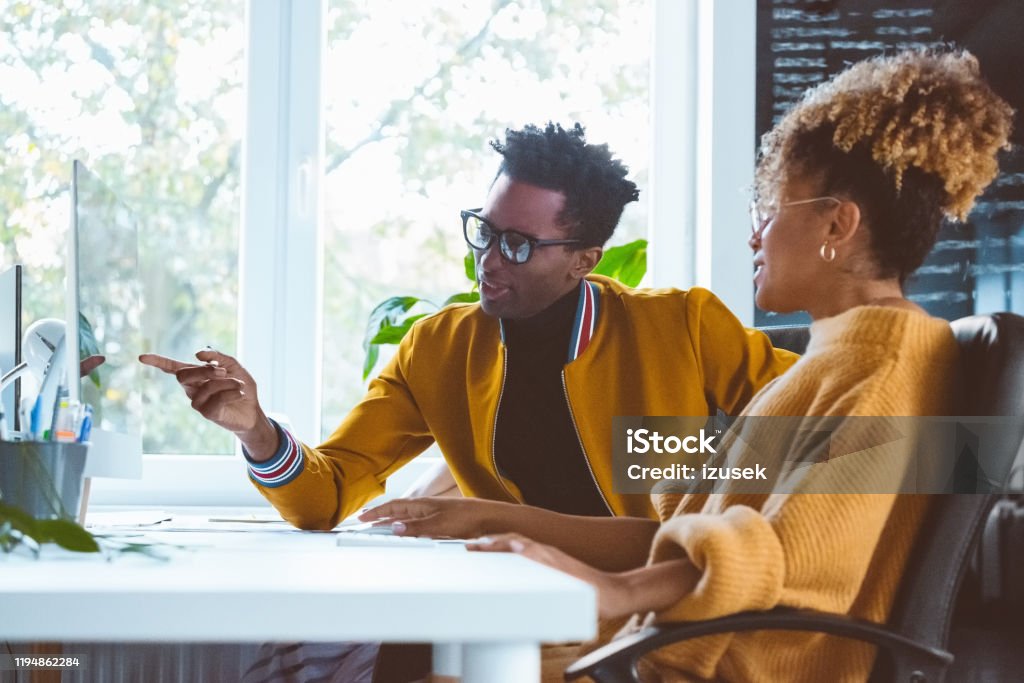 Business professionals discussing over a project in office African businessman pointing at computer monitor and discussing with businesswoman. Male and female business processionals in casuals discussing over a project in office. Explaining Stock Photo