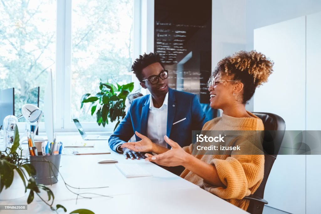 Business executives discussing in office Confident businesswoman discussing work with male colleague while working in office. Male and female executives in casuals discussing at desk in office. 30-34 Years Stock Photo