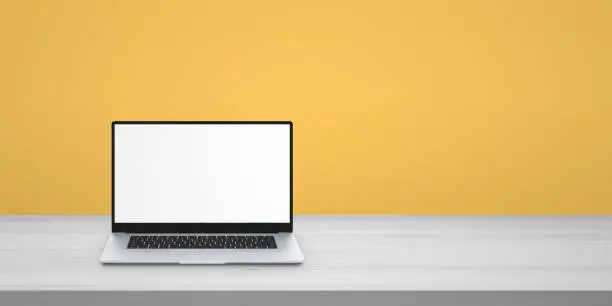 Laptop on desk with copy space beside. Isolated screen for mockup. Yellow wall in background