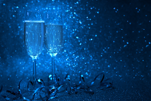 Two glasses of champagne decorated streamers on blue glittering background. Christmas and New Year holidays concept. Copy space.