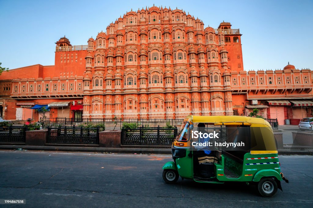 Indian man drives auto rickshaw (tuk-tuk), India Indian man drives auto rickshaw (tuk-tuk) on streets of Rajasthan, India. Hawa Mahal (The Wind Palace) on the background. India Stock Photo